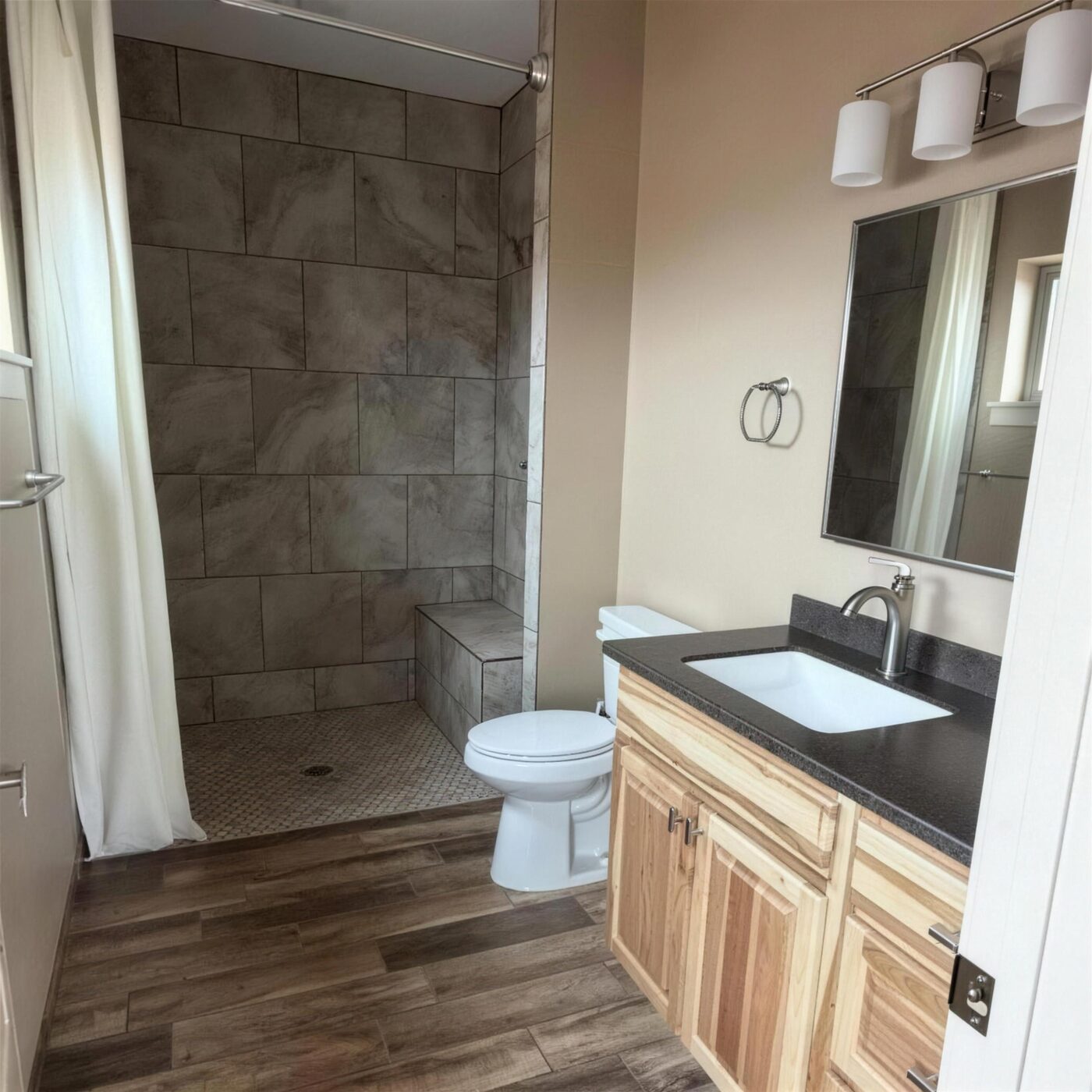 A finished bathroom remodel with a tiled walk-in shower with a built-in bench, a vanity with a dark countertop, and wood-look flooring.